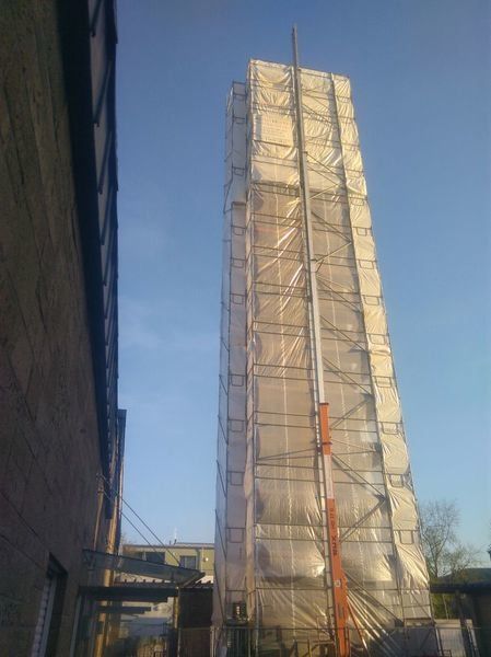 Eingehauster Gerüstturm im tief stehenden Abendlicht, neben einer dunklen Gebäudekante